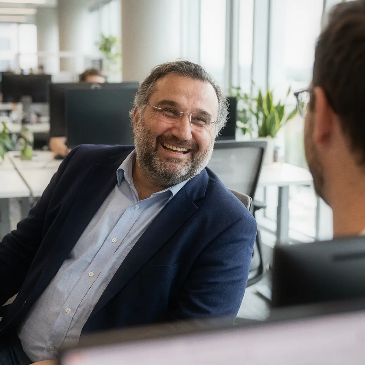 Sezgin Arslan laughing in conversation with a colleague in a bright open-plan office